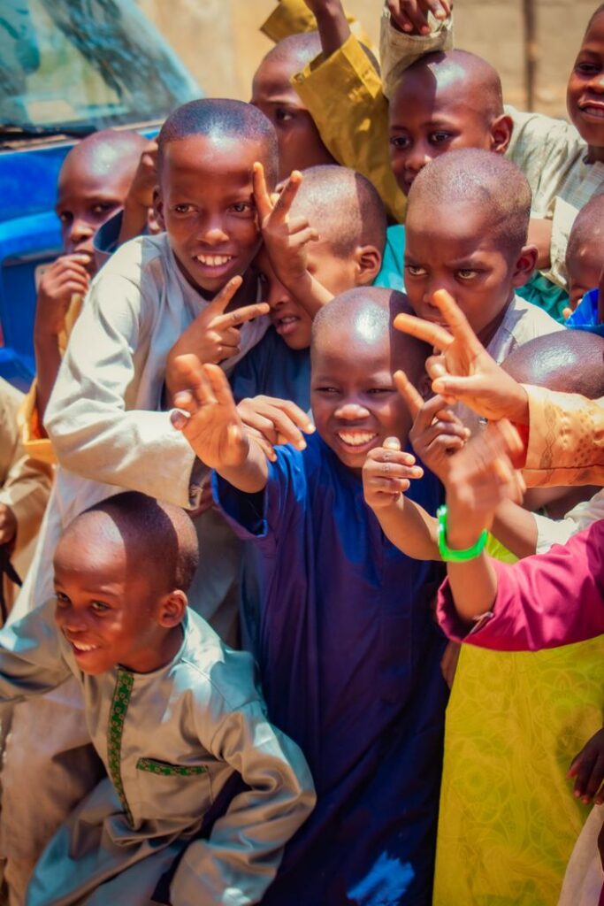 A lively group of children smiling and posing outside on a sunny day, exuding happiness and playfulness.