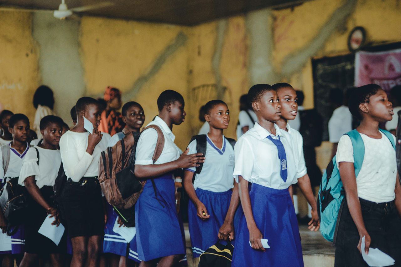 Group of African high school girls in uniform during class transition indoors.